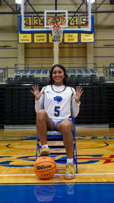Rosie Pastrano @Rosie_Pastrano A young athlete in a basketball uniform sits on a chair, holding a basketball and smiling.
